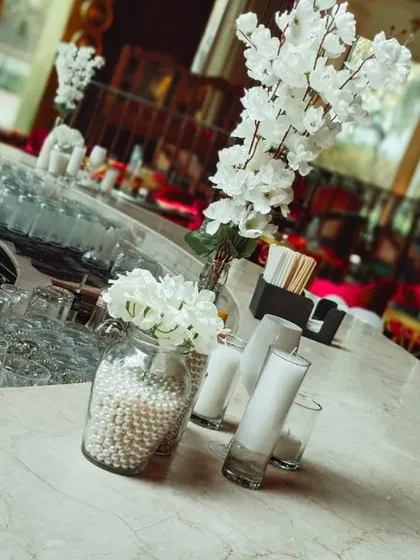 An elegant white-themed centerpiece arrangement on a marble countertop, featuring white flowers and candles.