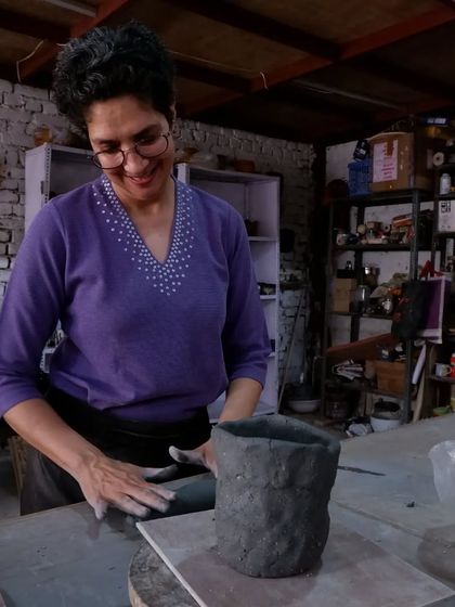 A smiling student smoothing the walls of her hand-built pot. The joy of the process is evident in her expression.