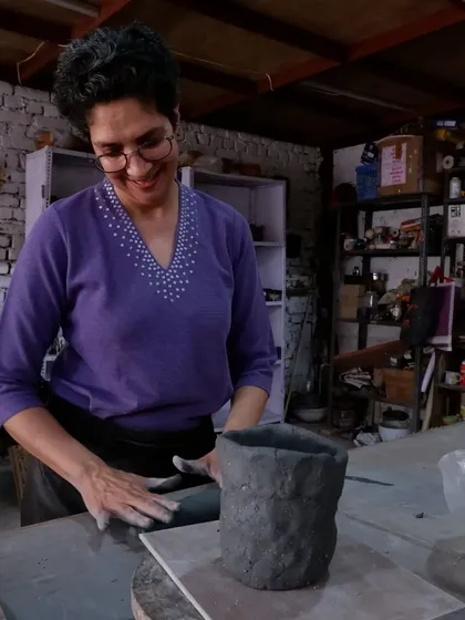 A smiling student smoothing the walls of her hand-built pot. The joy of the process is evident in her expression.