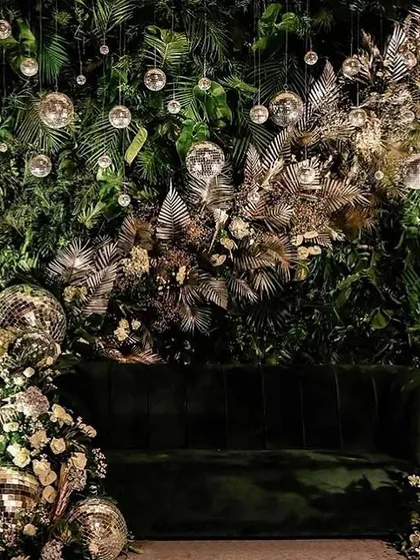 We love blending modern aesthetics with natural elements. This unique reception backdrop features a lush green wall, accented with metallic fronds and sparkling disco balls, creating a chic and glamorous photo opportunity.