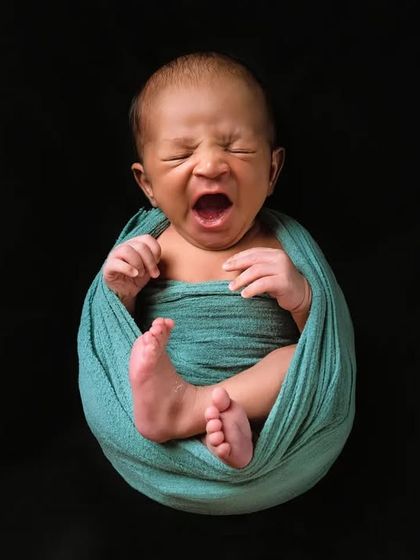 A big yawn from a tiny baby. This shot captures a classic newborn expression, showing the baby suspended in a hanging wrap pose.