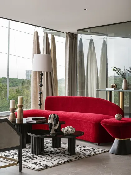 A bold statement in our studio, this vibrant red curved sofa is set against floor-to-ceiling windows. This vignette showcases how I use daring color and sculptural furniture to create focal points, with fabric samples on display to illustrate the customization process.