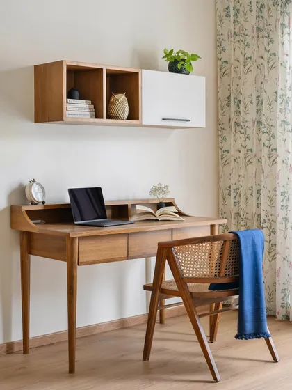 A modern Indian vibe defines this study nook in the 'House of Kismish' project. The space features a sleek wooden desk with elegant tapered legs and a floating overhead storage unit.