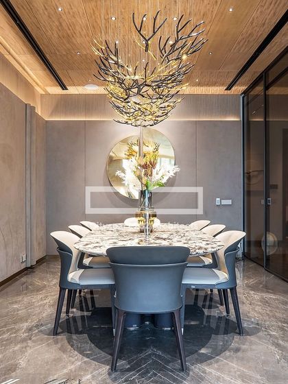 This luxurious dining area is defined by a sleek marble-topped table and a stunning nature-inspired chandelier. A large round mirror reflects the light and adds depth, while the muted color palette creates a refined and elegant atmosphere for togetherness.