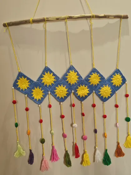 A closer look at the sun-themed crochet wall decor. This piece is hung on a natural wood branch and features colorful tassels and beads.
