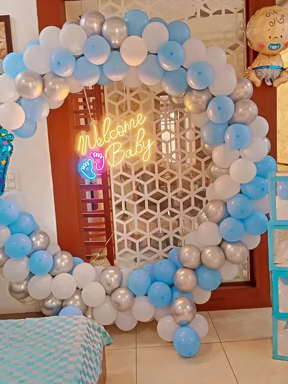 I create stunning welcome home decorations for baby boys, like this full balloon ring in shades of blue, white, and silver. The setup is completed with a "Welcome Baby" neon sign, "BABY" display boxes, and themed foil balloons.