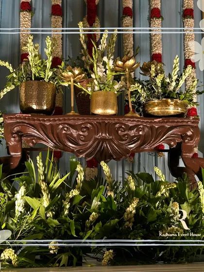 A close-up of a vintage-style carved wooden table, surrounded by fresh tuberose arrangements in brass pots.