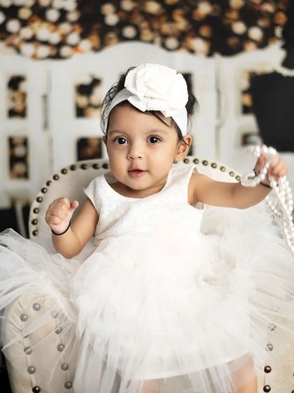 Playing with a string of pearls, this little girl is the picture of glamour in her beautiful white dress.