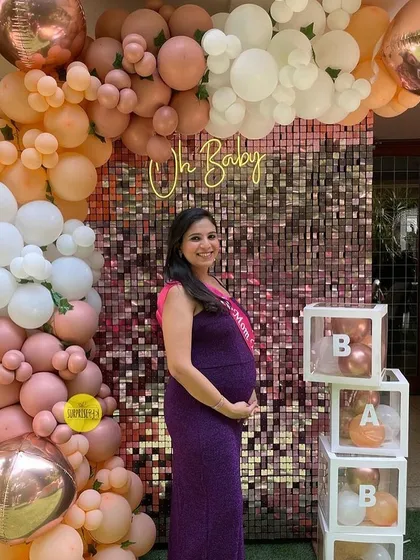 An elegant "Oh Baby" backdrop for a baby shower. This setup features a shimmering sequin wall framed by a cascade of peach, pink, and white balloons, along with transparent "BABY" boxes.