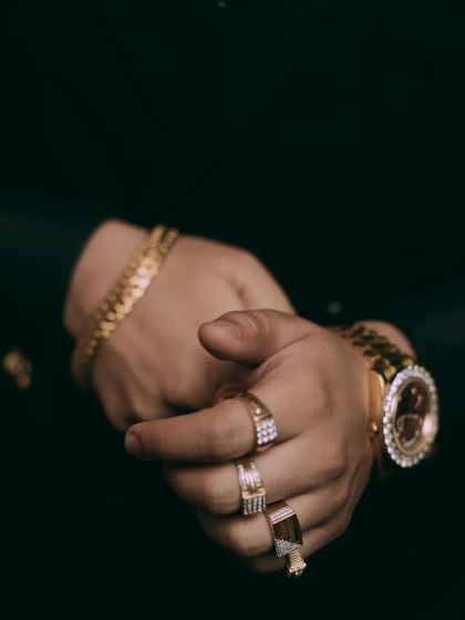 A detail shot focusing on the groom's hands, adorned with bold gold rings and a statement watch. This image is about capturing the style and personality that accessories bring to the groom's overall look.