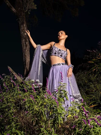 A magical, night-time fashion shoot in a field of lavender. The dramatic lighting creates a fairy-tale atmosphere, making the lavender lehenga seem to glow.