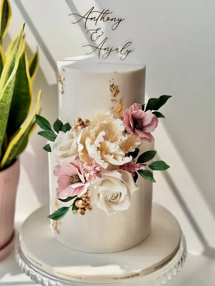 Learn to craft breathtaking floral arrangements with sugar. This elegant two-tiered anniversary cake, adorned with handmade sugar flowers and delicate gold leaf, is a perfect example of the romantic designs you can create.