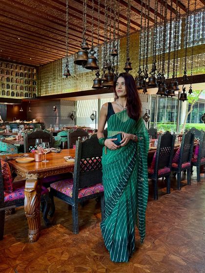 A solo shot of my Teej brunch look. The emerald green leheriya saree is paired with a simple black sleeveless blouse, which makes the traditional print feel modern and chic. The look is completed with a matching green clutch.
