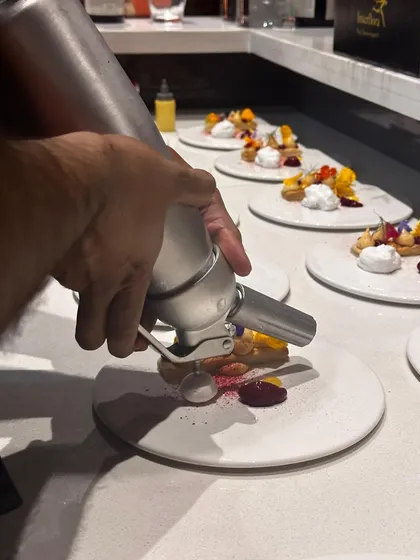 Another angle of the siphon in action, adding the finishing touch to a complex dessert plate.