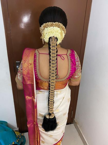 For this Muhurtham look, I created a classic braid adorned with traditional temple jewellery and a neat arrangement of jasmine flowers. This style is a perfect match for the bride's elegant white and pink silk saree.