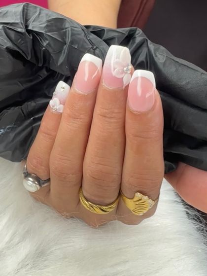 A close-up of a 3D ombre nail set, showing the delicate white flowers and pearl accents on a classic French tip base.