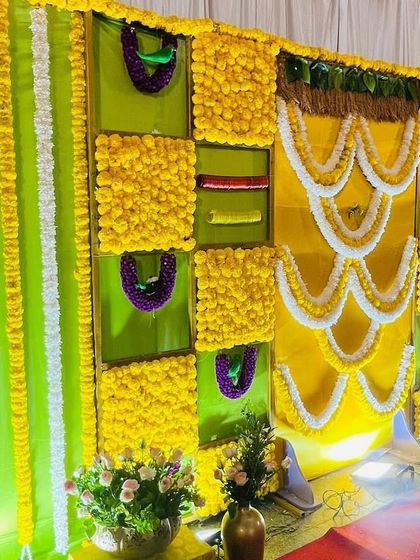 A bright and cheerful Seemantham backdrop with a yellow and green theme. The design features panels of marigolds and is decorated with intricate white floral garlands.