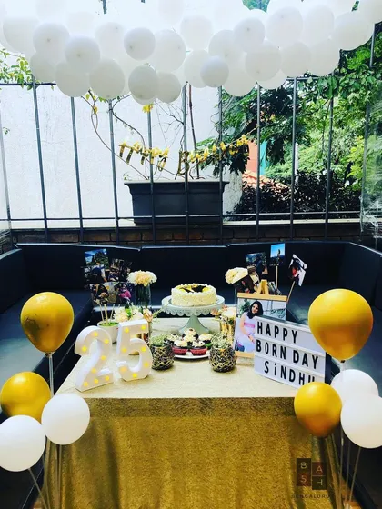 Celebrating a 25th birthday with sunshine and gold. This setup features a 'cloud' of white balloons overhead, a gold and white color scheme, and personalized elements like a 'Happy Born Day' lightbox and marquee numbers.