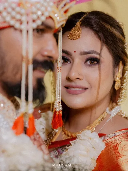A beautiful close-up of a bride looking directly at the camera, her face framed by the groom's turban. Her confident smile and radiant makeup make this a stunning bridal portrait.