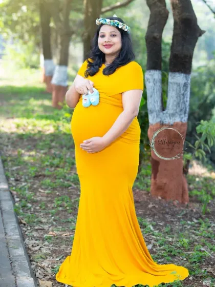 A full-length portrait showcasing a beautiful baby bump. The mom-to-be holds tiny blue shoes, hinting at the baby boy she is so excited to meet.