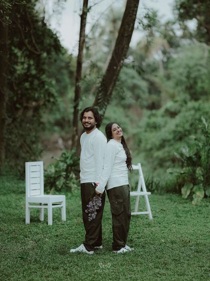 The couple standing back-to-back, holding a bouquet of purple flowers, a unique and sweet pose.