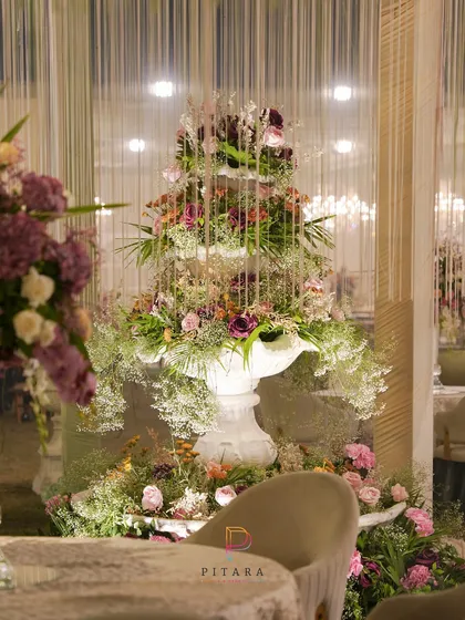 Another view of the magnificent floral fountain, showing how it anchors the space and creates a stunning focal point from every angle. The cascading threads of light add to the magical effect.