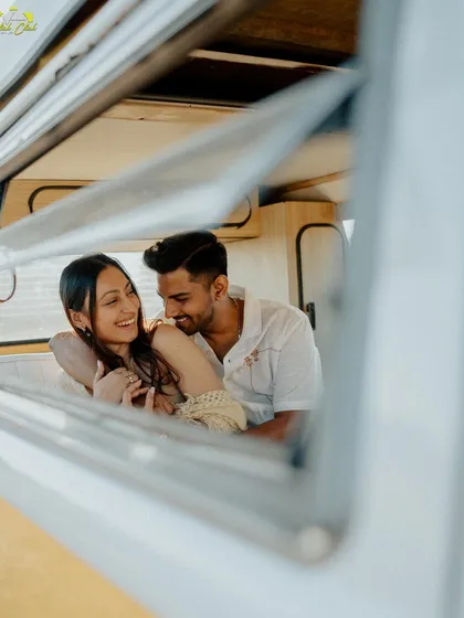 A creative shot through the window of the camper van, framing the couple's laughter and creating a sense of looking in on a private, happy moment.