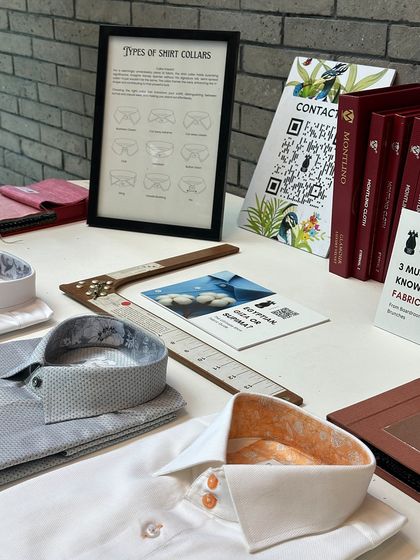 A detailed view of our shirting display at the BCG trunk show. We showcase shirts with unique details like contrasting inner collar fabrics, alongside educational charts explaining different collar types, empowering clients to make personalized choices.