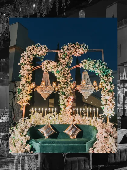A beautiful photo-op corner from the Sangeet, featuring a plush green sofa under a stunning arch of white flowers and crystal chandeliers. Every corner of the venue is designed to be picture-perfect.