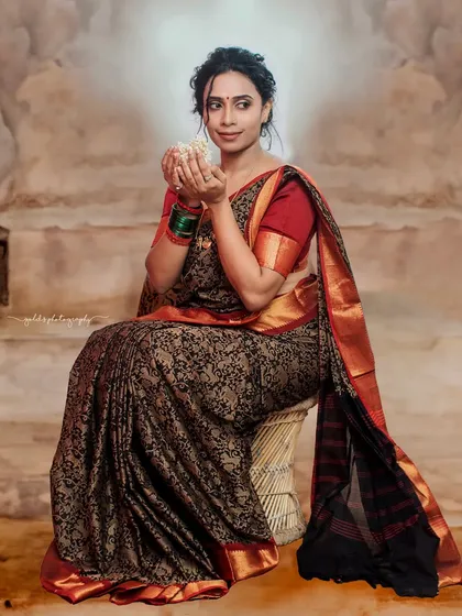 A full-length seated portrait that showcases the entire saree. The bride holds a jasmine flower, adding a traditional and fragrant touch to the image.