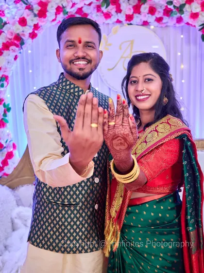 A couple in traditional green and red attire displaying their engagement rings. The shot captures their coordinated outfits and the joy of the moment.