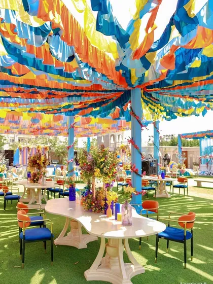 Colorful guest seating under a canopy of blue, yellow, and orange fabric strips. The unique tables and bold blue and orange chairs continue the vibrant, art-inspired theme.