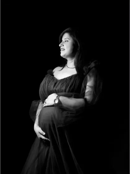 A classic black and white maternity portrait in a dark tulle gown, using studio lighting to create a timeless and elegant look.