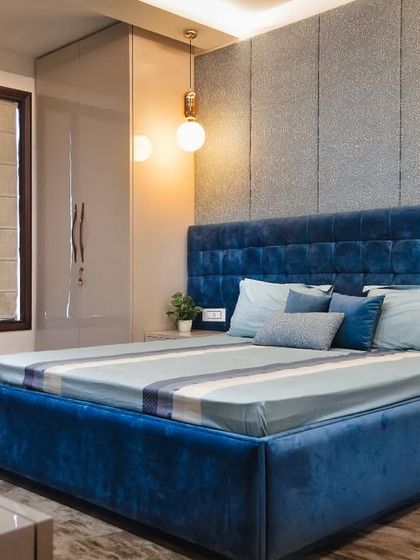 Another view of the blue-themed master bedroom, showcasing the full layout with a patterned armchair that adds a pop of interest and a sleek, glossy wardrobe.