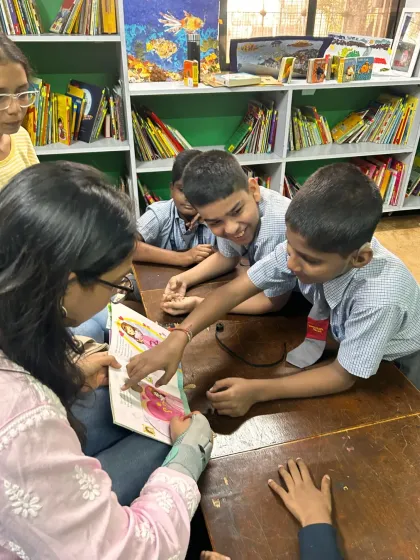 A volunteer shows a picture book to a group of boys, who lean in to get a closer look. These interactive moments are key to keeping children engaged and helping them connect with the visual elements of the story.