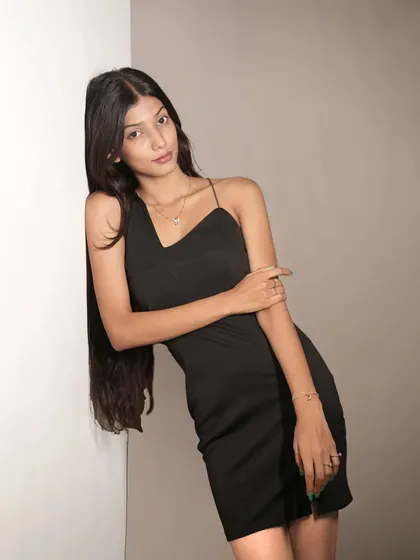 A relaxed yet confident pose, with the model leaning against a wall, showcasing the asymmetrical neckline of her dress.