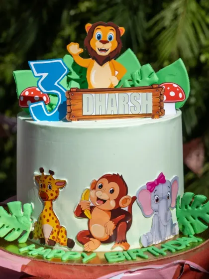 A cheerful animal themed cake for a third birthday, with a lion, monkey, giraffe, and elephant toppers set against a green jungle backdrop.