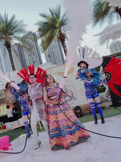 The couple makes a grand entrance at their carnival with CO2 guns, surrounded by performers in vibrant costumes. It's all about creating high-energy, memorable moments.