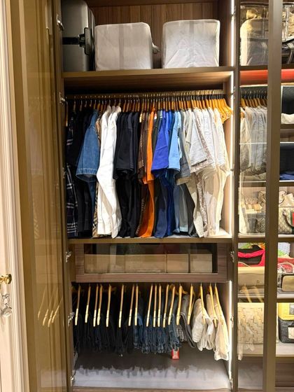This section of a walk-in closet features warm wood tones and integrated LED lighting. We used matching wooden hangers for a cohesive look and organized trousers on a lower pull-out rack for easy access.
