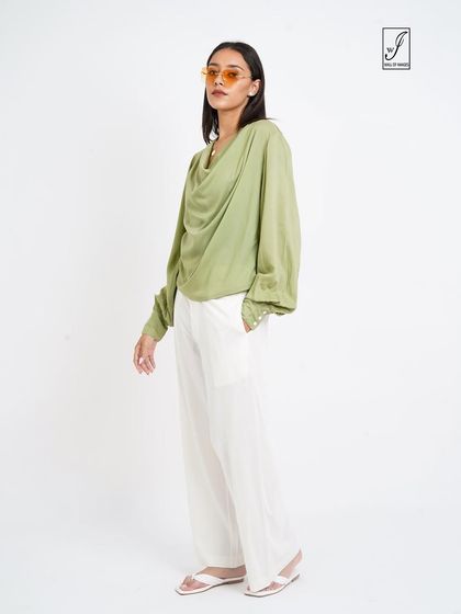 A chic look featuring a cowl-neck green top and white pants, perfect for a sophisticated fashion brand's catalogue.