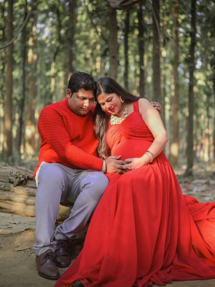 A quiet, intimate moment between expectant parents during their forest maternity shoot. The vibrant red of her dress contrasts beautifully with the natural surroundings.