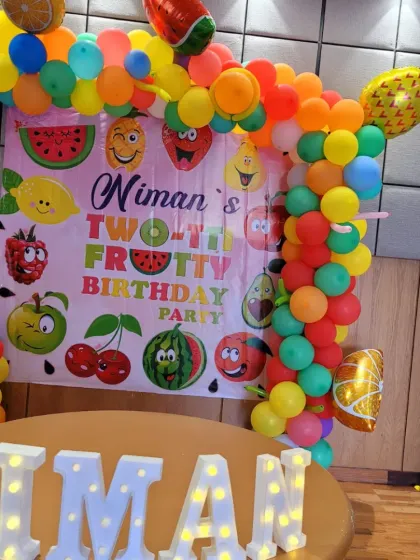 A fun and healthy "Two-tti Frutti" birthday party theme. The backdrop is filled with cheerful fruit characters, and the balloon arch uses a rainbow of colors to match the fruity concept.