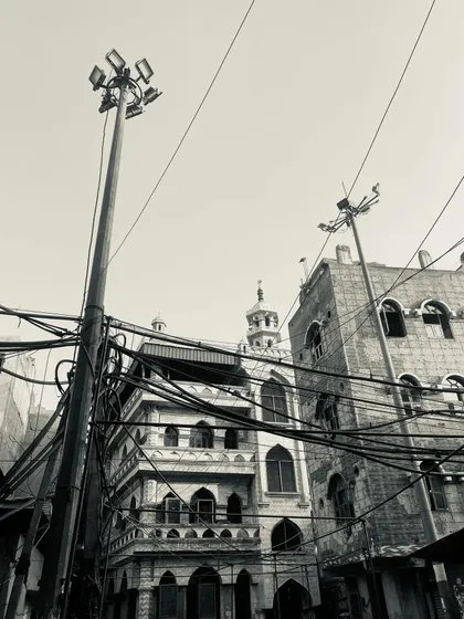 The contrast of old Mughal-style architecture with modern streetlights and electrical wires.