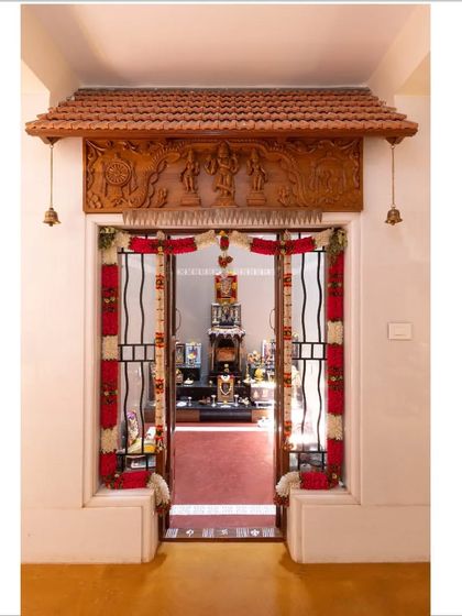 The entrance to the traditional puja room, framed by a carved wooden lintel and Mangalore tile awning, creating a sacred threshold within the contemporary home.
