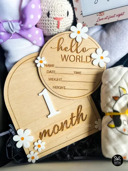 A detailed look at the wooden milestone cards, including a '1 month' plaque and a 'Hello World' birth announcement disc, decorated with cute daisy accents.