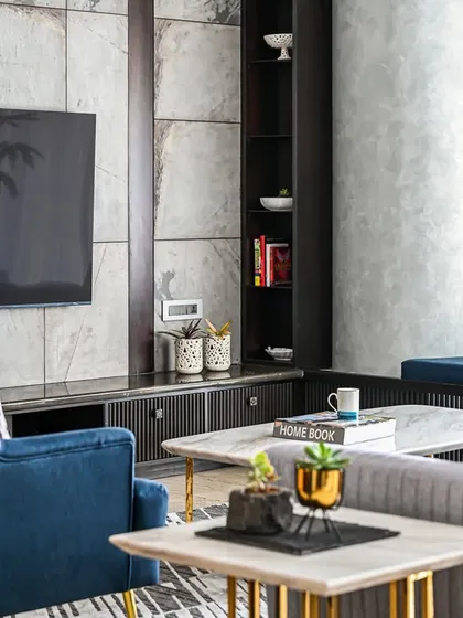 A closer view of the living area, highlighting the interplay of textures. The smooth, cool marble of the coffee tables contrasts with the soft velvet of the blue armchair and the textured grey paint on the structural column.