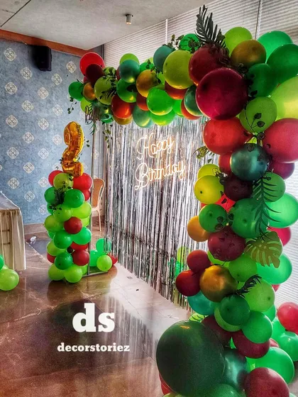 A side view of a jungle-themed balloon arch in a restaurant, showing how I can adapt large-scale decorations to different venues. The setup includes a neon sign and a balloon column for the age.