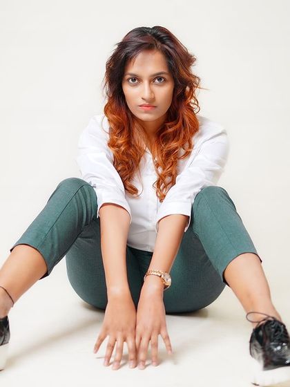 A modern, powerful seated pose on the studio floor. The combination of a classic white shirt with casual trousers and platform shoes creates a contemporary look.