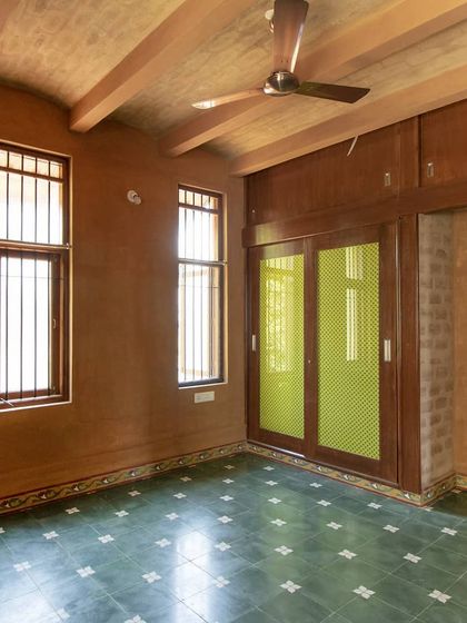A bedroom with mud walls, a jack arch roof, and green Athangudi floor tiles, creating a cool and earthy retreat.