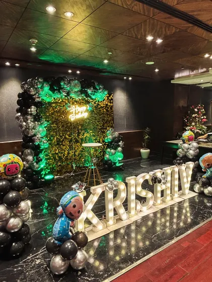 A grand setup in a hall with a green sequin wall and black and silver balloons. The large marquee letters spelling out 'Krishiv' make a bold statement.